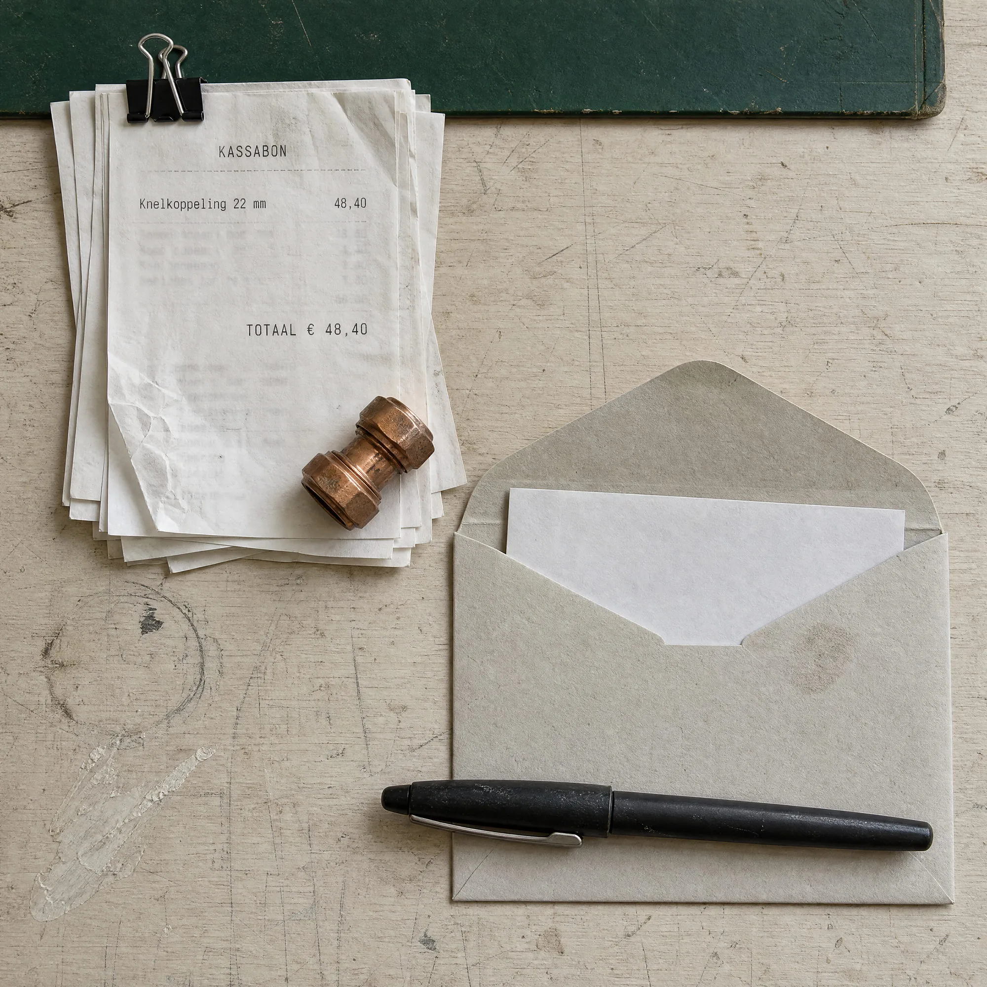 Een stapel kassabonnen met een koperen koppeling erop, een open envelop en een zwarte pen op een werkbank